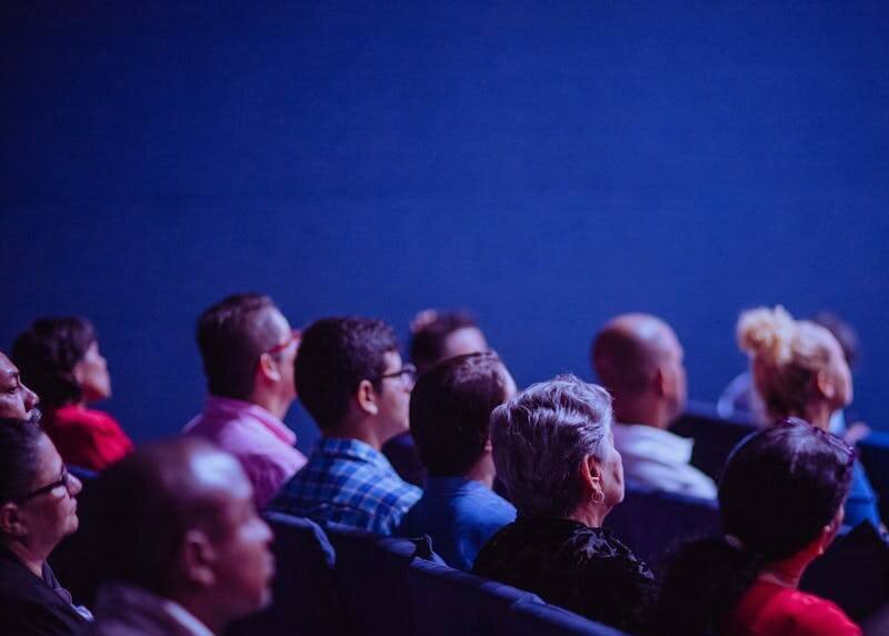 An attentive group of adults seated at an indoor conference, focusing on a presentation.